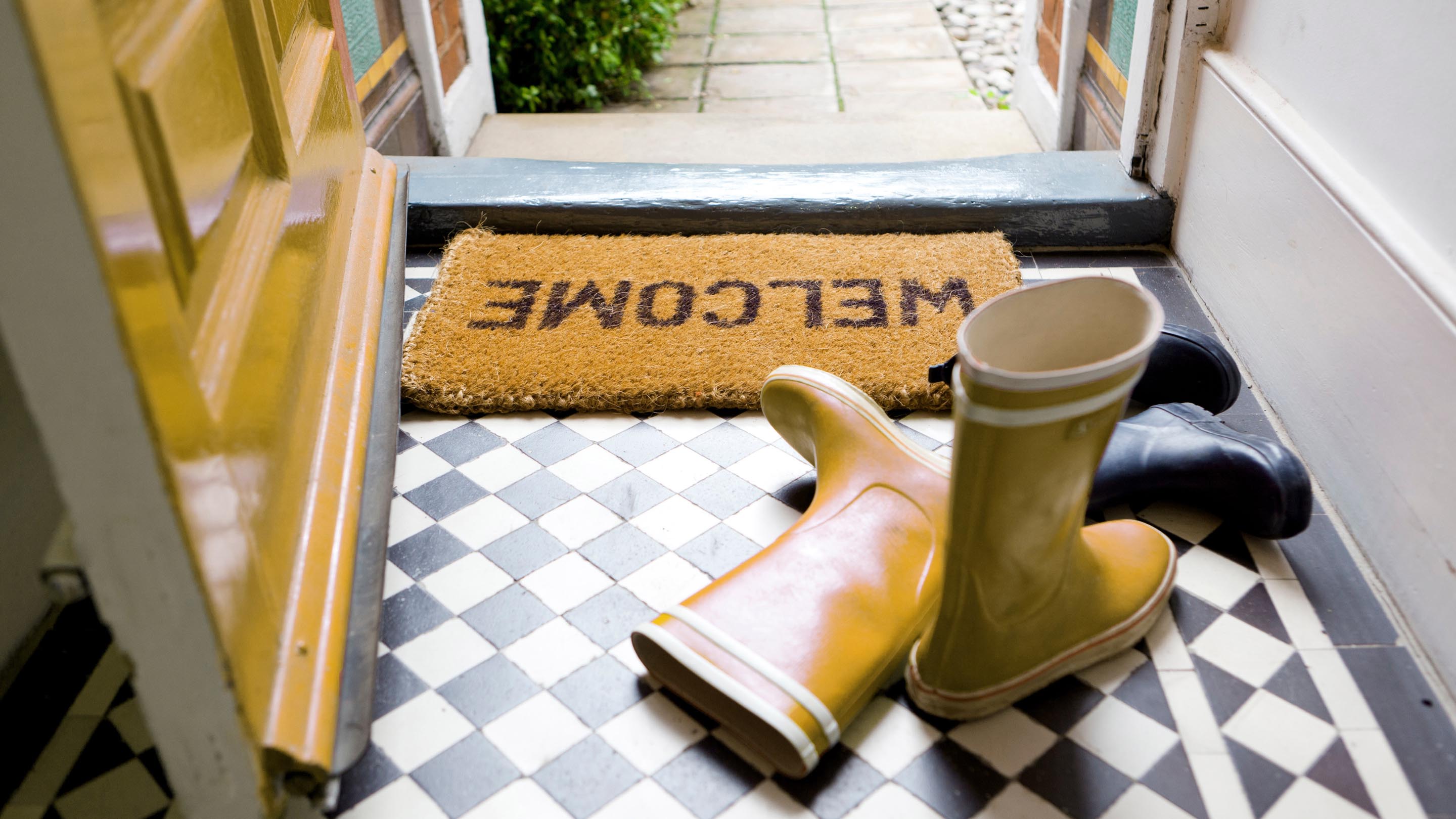 Yellow wellington boots placed by a front door and welcome mat